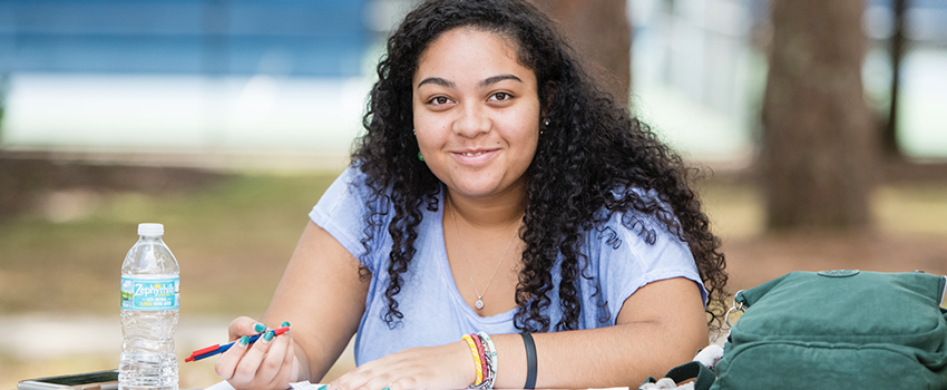 Female student writing in notebook sitting outside on campus.