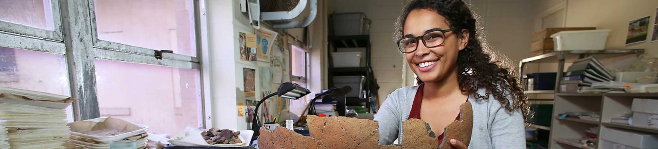 Female student holding an artifact in a lab.