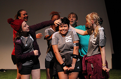 Students in soccer uniforms performing a play.