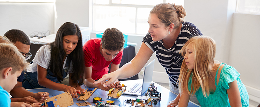 Teacher working with students on project at table.