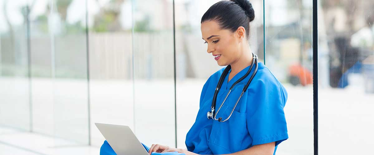 Healthcare worker sitting on floor typing on laptop.
