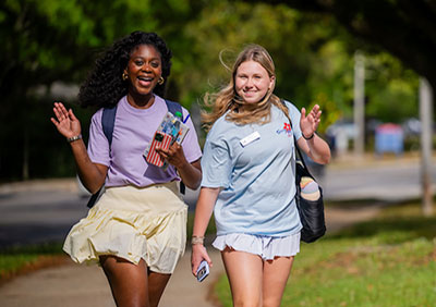 Two students waving on campus.