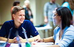 A male and female student working on laptops smiling