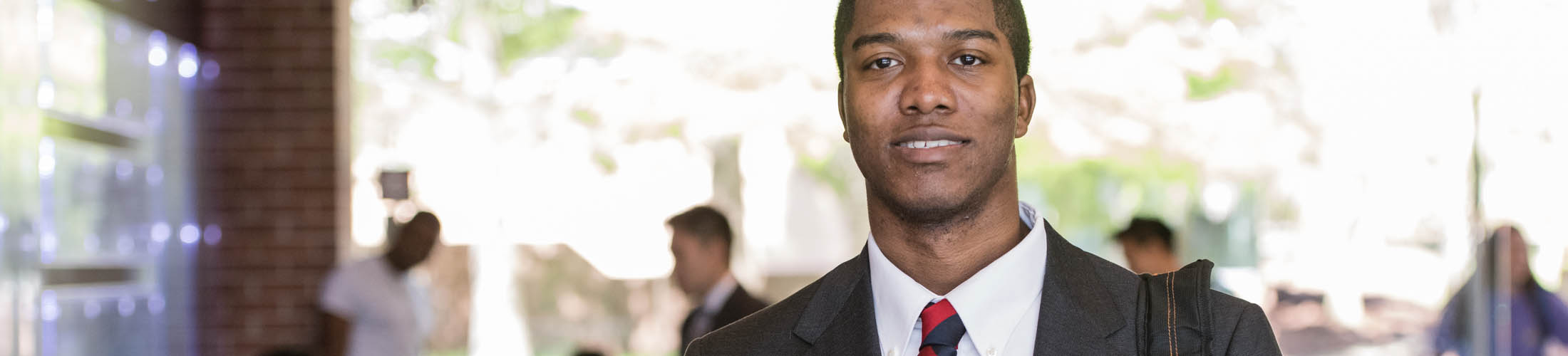 Male student dressed in a suit walking outside on campus.