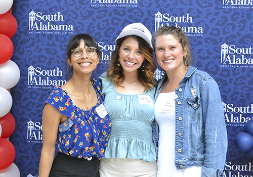 Three alumni members in front of South backdrop smiling.