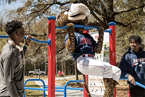 Southpaw doing a pull up on the Jag Fitness trail while students watch.