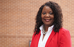 Female wearing red blazer in in front of brick wall 