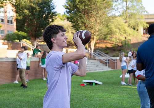 Student playing corn hole outside at an IFC event.