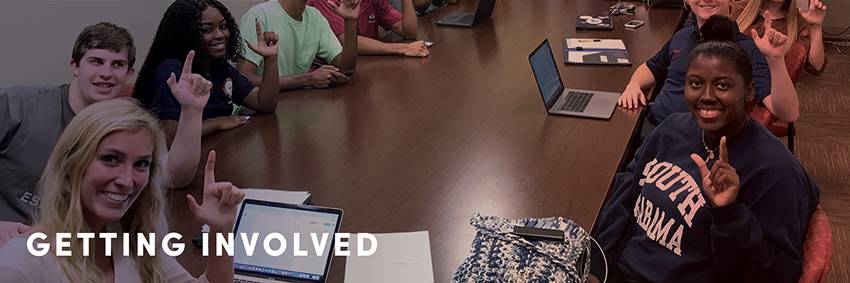 Student RAs sitting around conference table holding up J sign