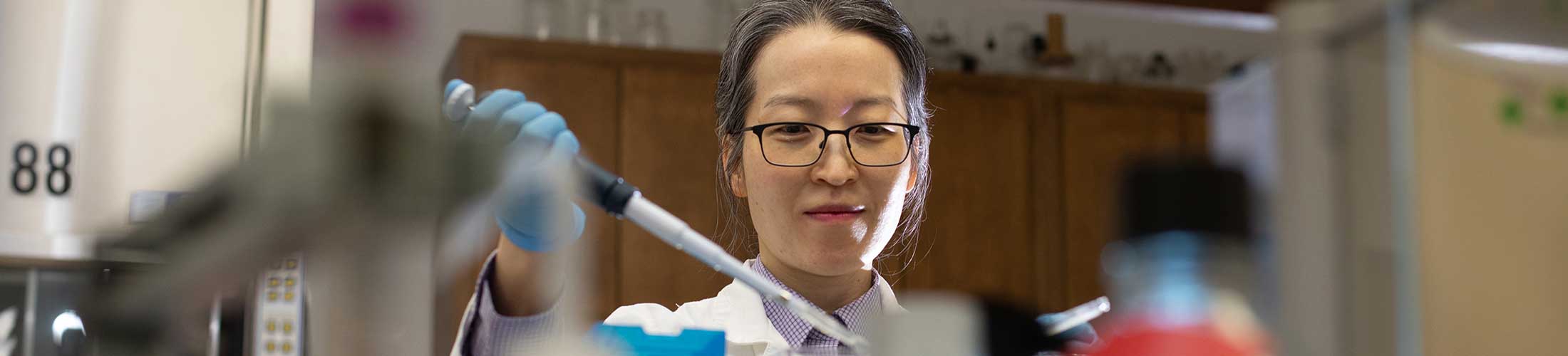 Researcher working in the lab holding a dropper with gloves on.