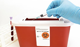 Hand putting needle in biohazard box